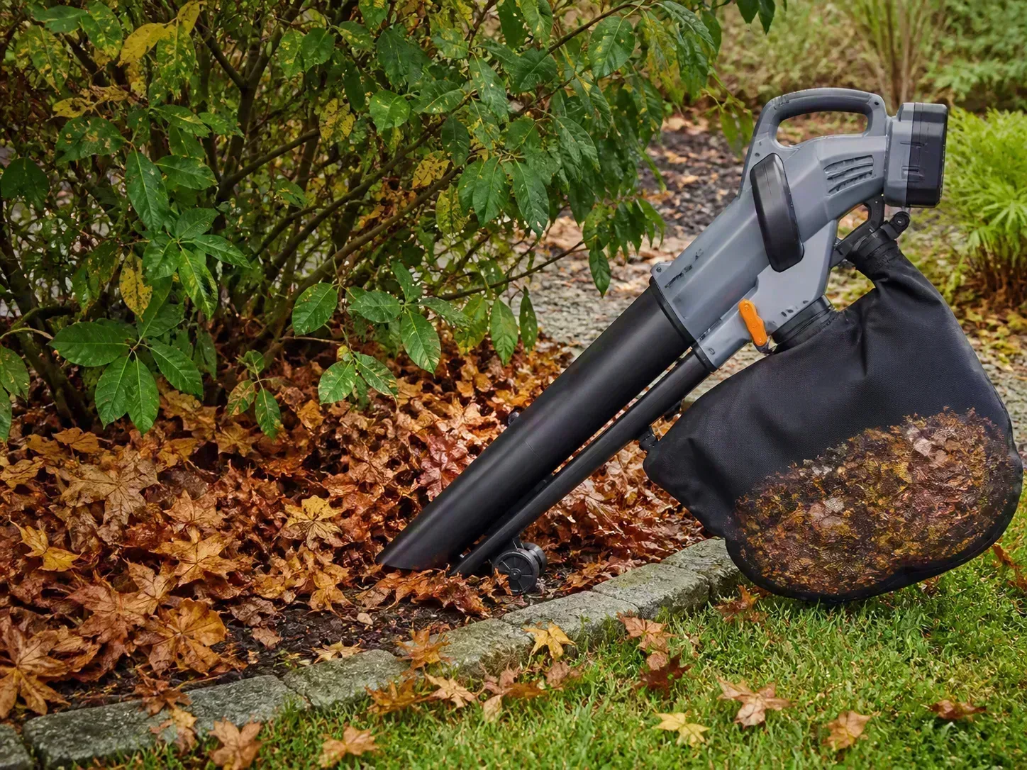 A leaf mulcher collecting autumn leaves beside a garden bed