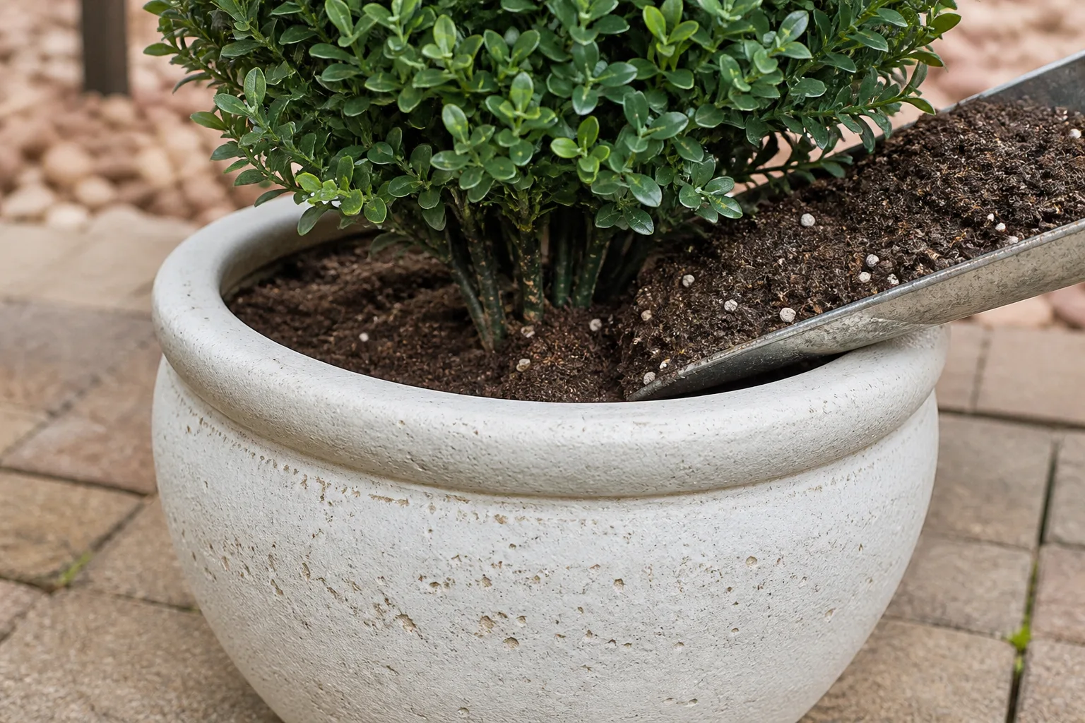 Heavy patio planter filled with potting soil anchoring the base of artificial greenery stems