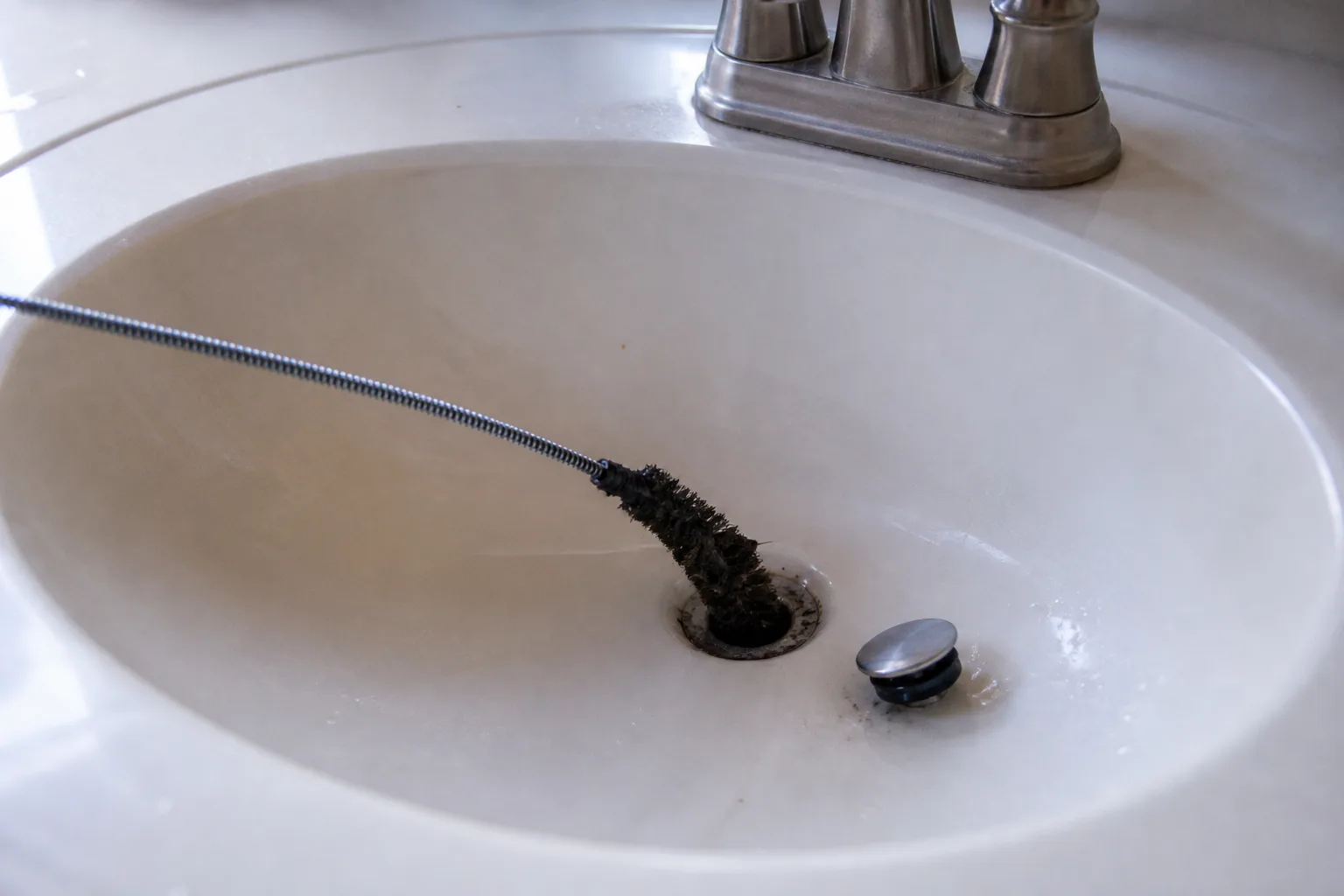 A dedicated brush cleaning the accessible area around a sink drain