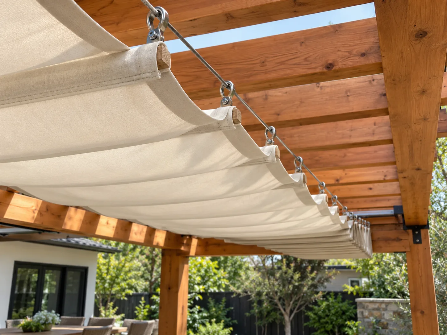 Retractable fabric panels gathered on sliding carriers beneath a pergola.