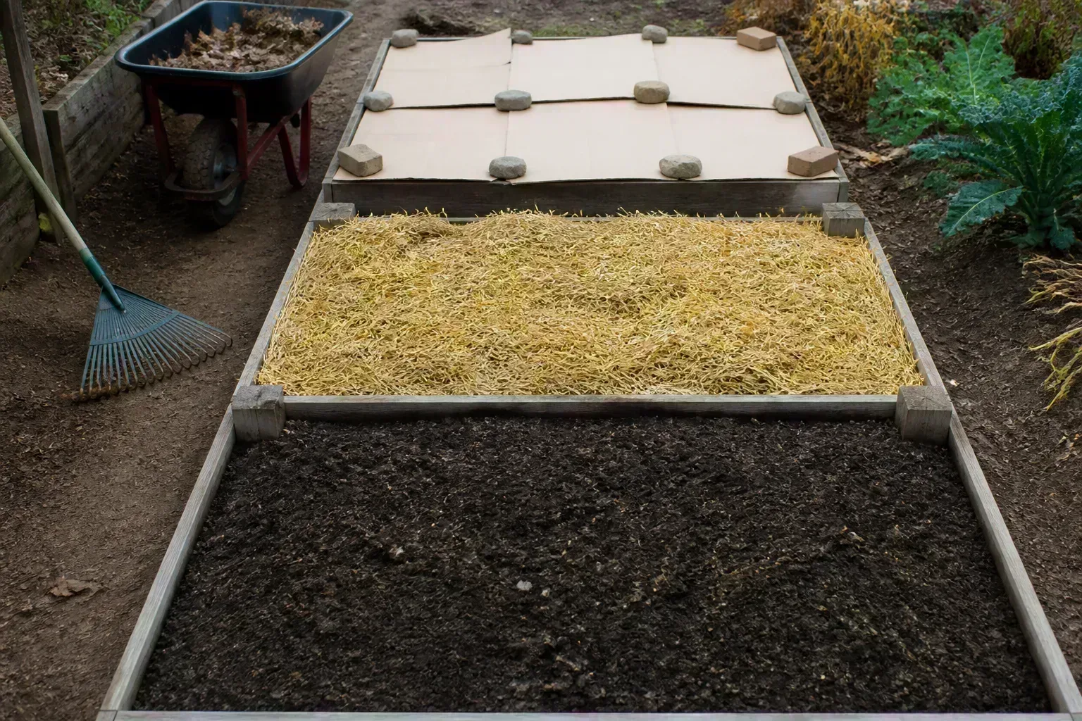 A raised garden bed protected with leaf mulch and breathable covers before winter weather arrives